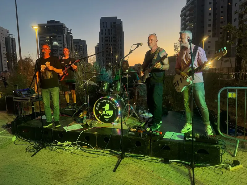 להקת אקרופוליס על במה פתוחה בשעת שקיעה, עם בניינים ברקע